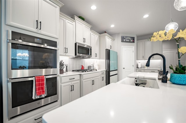 kitchen featuring tasteful backsplash, stainless steel appliances, sink, white cabinetry, and hanging light fixtures