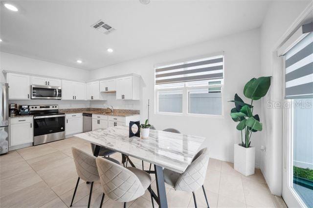 kitchen with light stone countertops, appliances with stainless steel finishes, light tile patterned floors, and white cabinetry