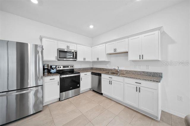 kitchen featuring white cabinetry, sink, dark stone countertops, light tile patterned floors, and appliances with stainless steel finishes