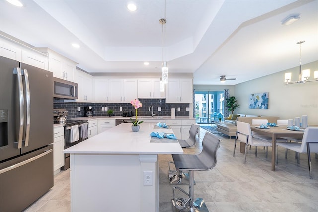 kitchen with a kitchen island, white cabinets, decorative light fixtures, and appliances with stainless steel finishes