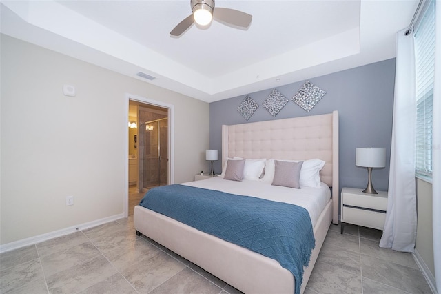 bedroom with ensuite bath, a raised ceiling, and ceiling fan