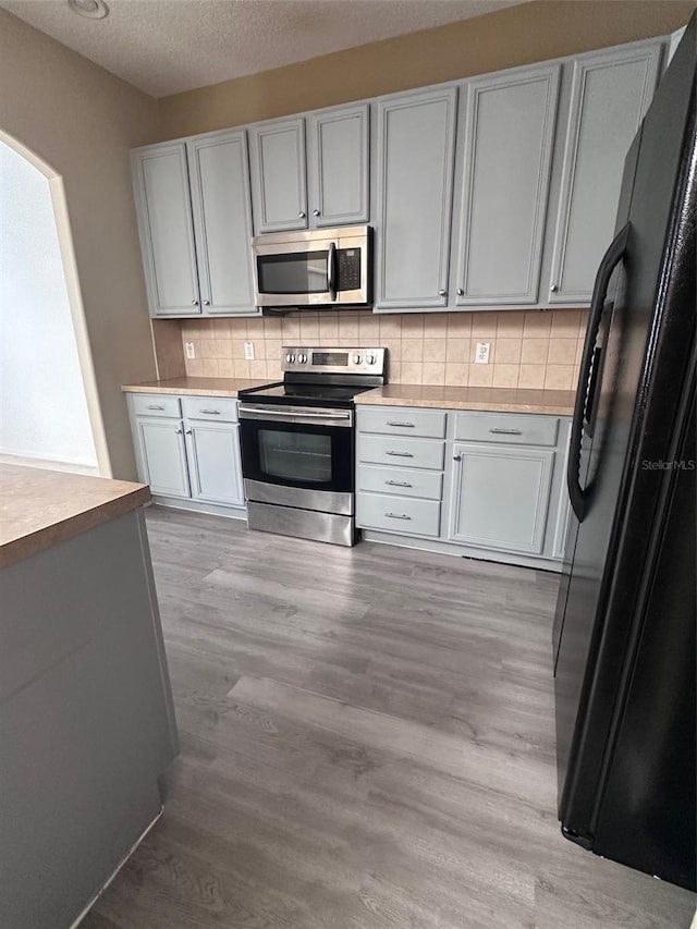 kitchen with tasteful backsplash, a textured ceiling, stainless steel appliances, white cabinets, and light hardwood / wood-style floors