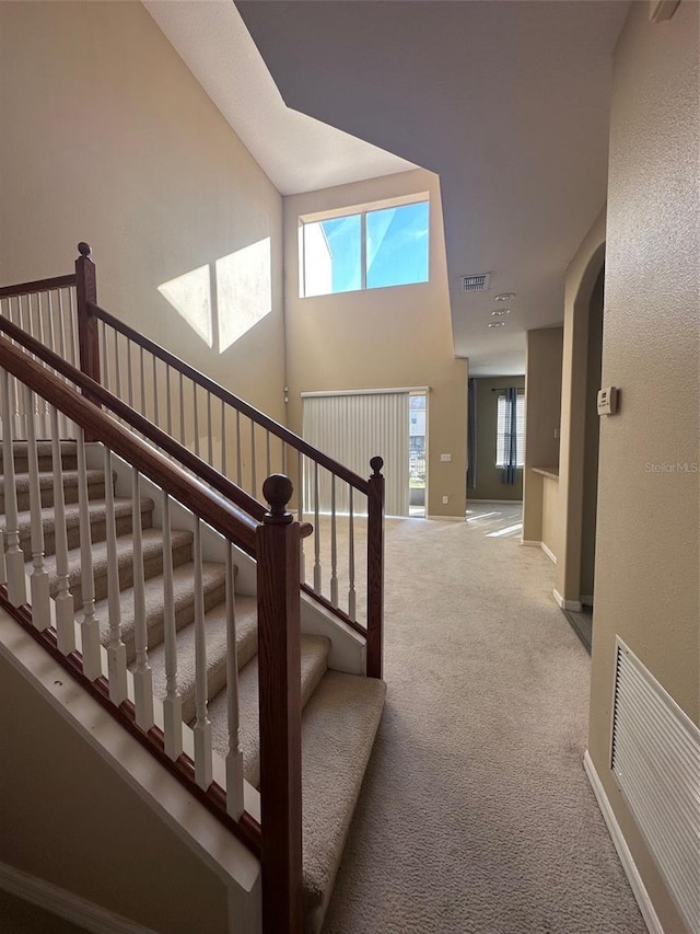 stairway with carpet flooring and a towering ceiling