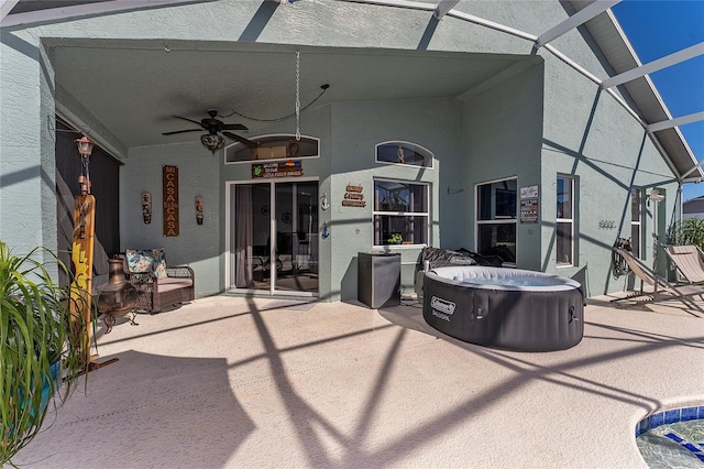 view of patio / terrace featuring a hot tub, glass enclosure, and ceiling fan