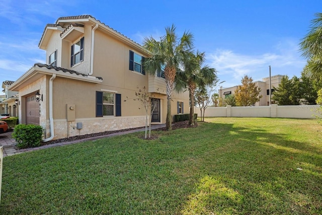 rear view of property with a garage, fence, a tiled roof, a lawn, and stucco siding