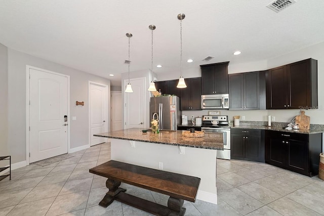 kitchen featuring stainless steel appliances, a breakfast bar, visible vents, an island with sink, and dark stone countertops