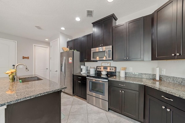 kitchen with a textured ceiling, sink, light stone countertops, and stainless steel appliances