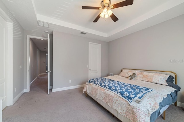 carpeted bedroom with a ceiling fan, a tray ceiling, visible vents, and baseboards