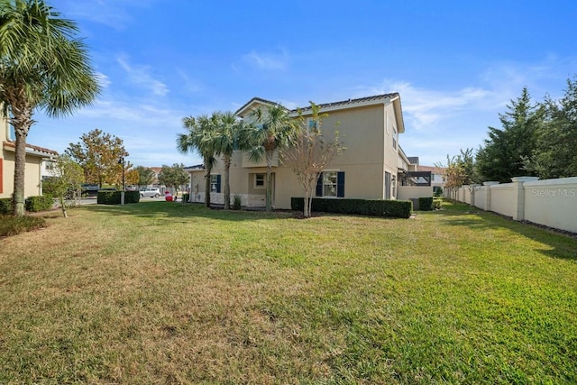 rear view of house featuring stucco siding, fence, and a lawn