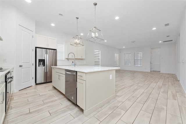 kitchen with pendant lighting, a center island with sink, white cabinets, light hardwood / wood-style floors, and stainless steel appliances