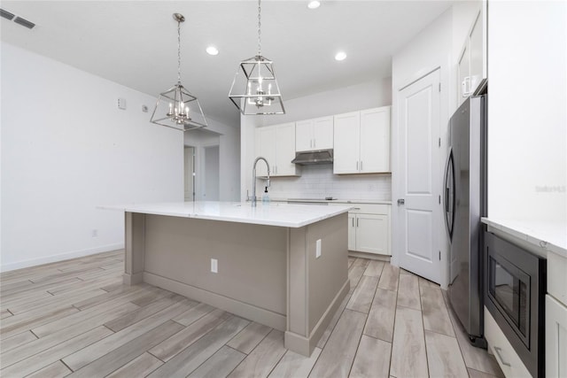 kitchen featuring pendant lighting, white cabinets, light hardwood / wood-style flooring, an island with sink, and stainless steel appliances