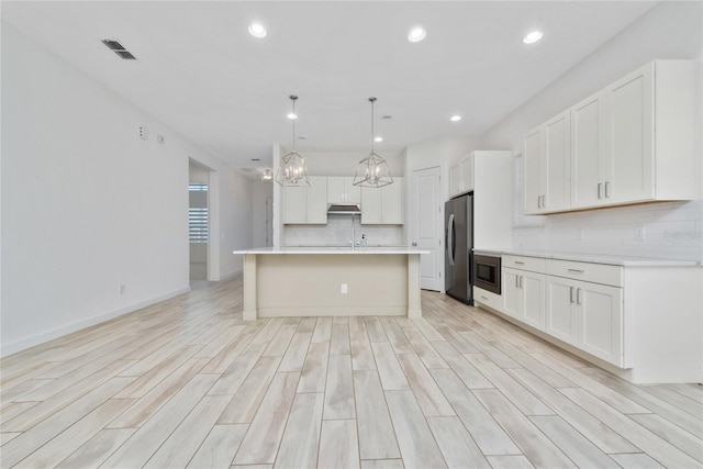 kitchen featuring appliances with stainless steel finishes, a kitchen island with sink, decorative light fixtures, light hardwood / wood-style flooring, and white cabinets