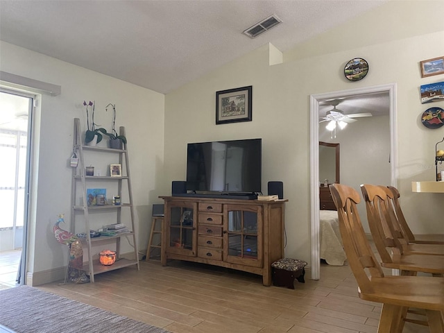 living room featuring ceiling fan, lofted ceiling, a textured ceiling, and light hardwood / wood-style flooring