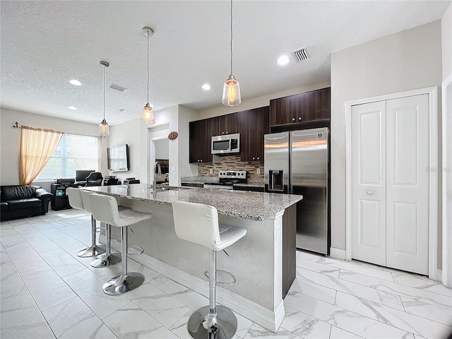 kitchen featuring light stone countertops, appliances with stainless steel finishes, backsplash, a kitchen breakfast bar, and an island with sink