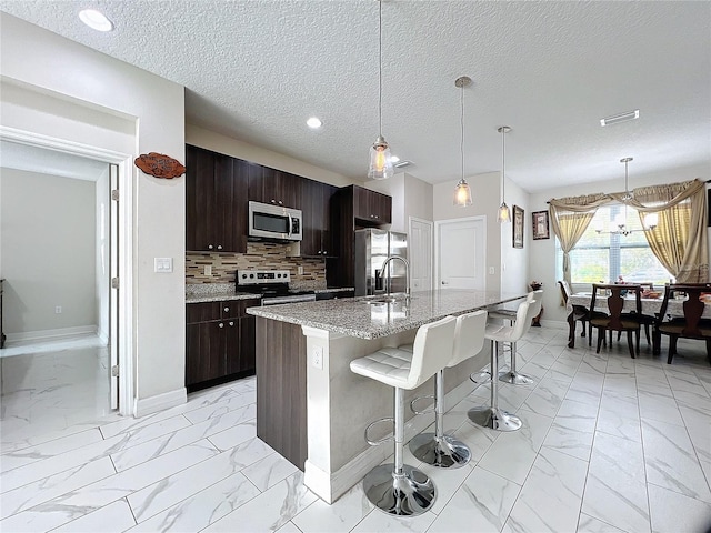 kitchen with decorative backsplash, dark brown cabinetry, stainless steel appliances, and an island with sink