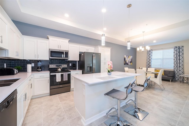 kitchen featuring white cabinets, stainless steel appliances, a raised ceiling, and hanging light fixtures