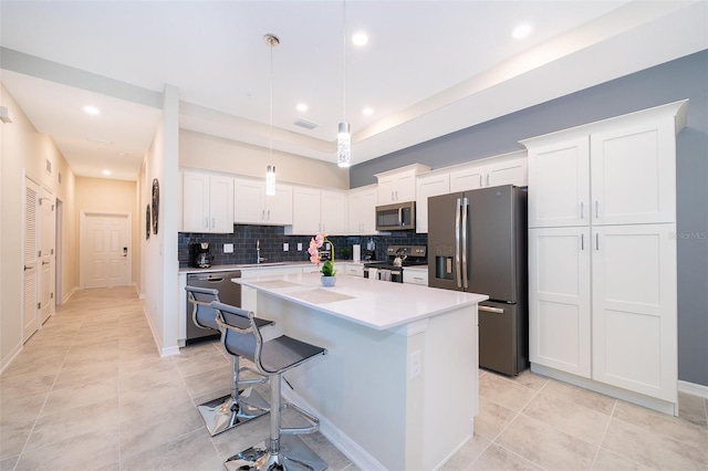 kitchen featuring appliances with stainless steel finishes, decorative light fixtures, white cabinetry, and a kitchen island