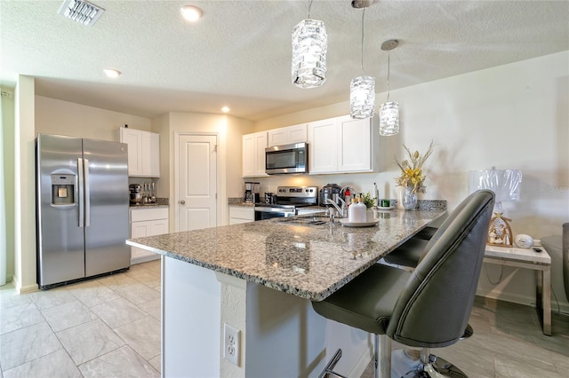 kitchen with kitchen peninsula, appliances with stainless steel finishes, a breakfast bar, pendant lighting, and white cabinets