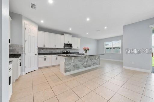 kitchen with white cabinets, light tile patterned floors, backsplash, and an island with sink