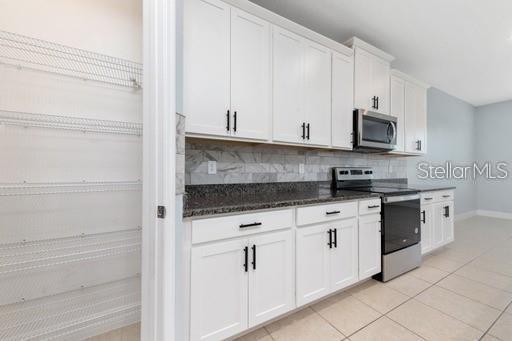 kitchen featuring dark stone counters, white cabinets, appliances with stainless steel finishes, tasteful backsplash, and light tile patterned flooring