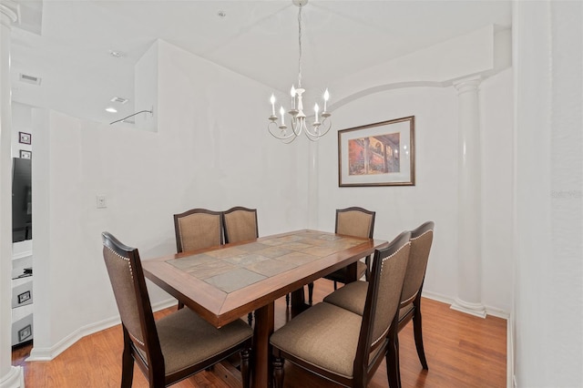 dining area with decorative columns, light wood-type flooring, and a chandelier