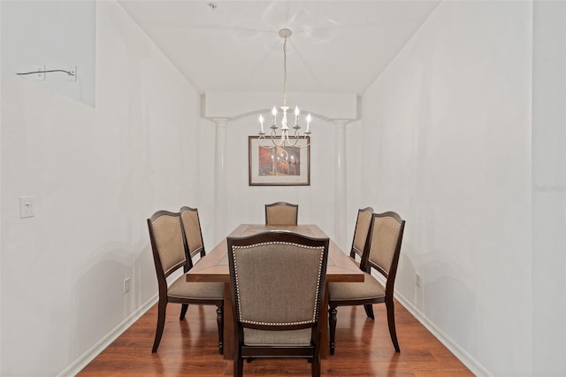 dining space with ornate columns, a notable chandelier, and hardwood / wood-style flooring