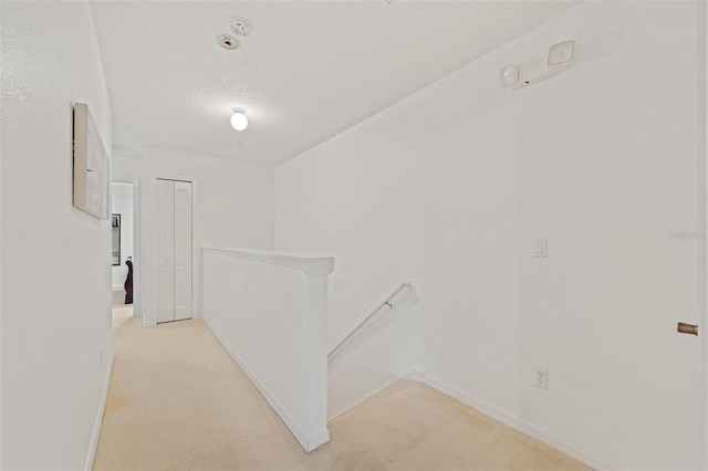 hall with light carpet and a textured ceiling