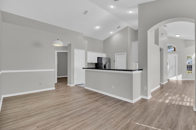 kitchen featuring white cabinets, light wood-type flooring, stainless steel refrigerator with ice dispenser, and high vaulted ceiling