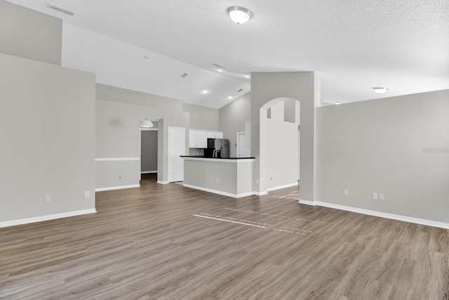 unfurnished living room with a textured ceiling, high vaulted ceiling, and light hardwood / wood-style flooring