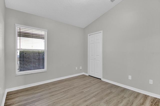 spare room with a textured ceiling, light hardwood / wood-style flooring, and lofted ceiling