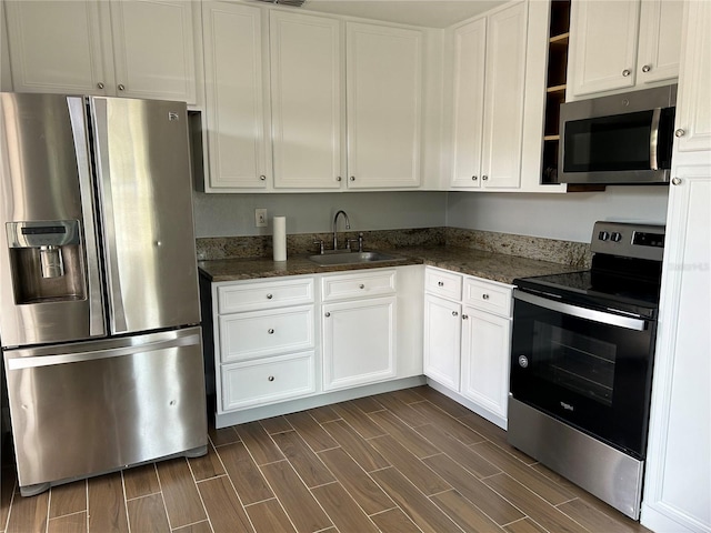 kitchen featuring white cabinets, sink, dark hardwood / wood-style floors, dark stone countertops, and appliances with stainless steel finishes