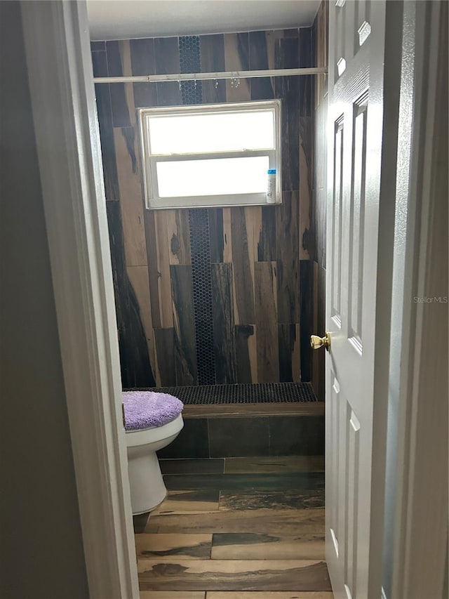 bathroom with hardwood / wood-style flooring, toilet, and a tile shower