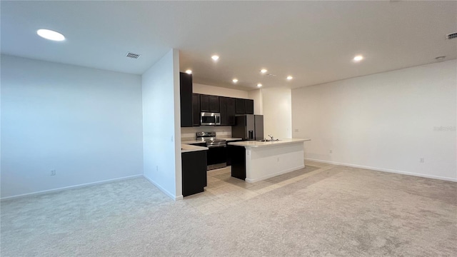 kitchen with appliances with stainless steel finishes, light colored carpet, and an island with sink