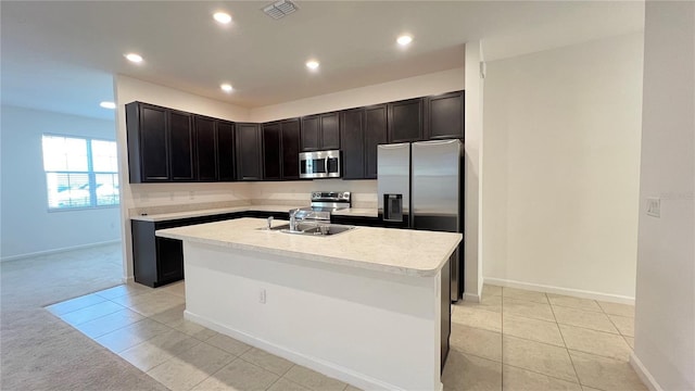 kitchen with appliances with stainless steel finishes, a center island with sink, light tile patterned floors, and sink