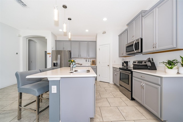 kitchen with gray cabinetry, a breakfast bar, a kitchen island with sink, sink, and stainless steel appliances