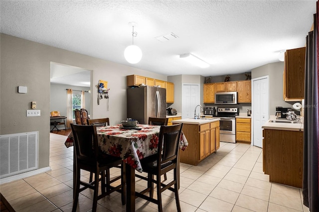 kitchen featuring a textured ceiling, stainless steel appliances, pendant lighting, a center island with sink, and light tile patterned flooring