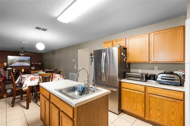 kitchen with stainless steel fridge, a textured ceiling, ceiling fan, sink, and an island with sink