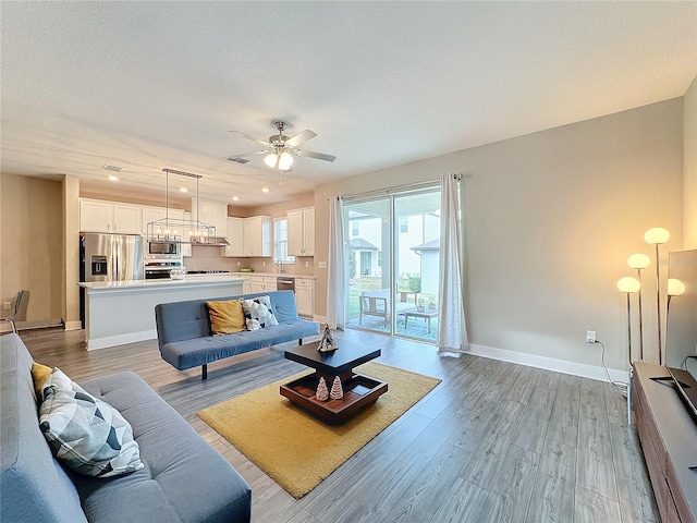 living room with ceiling fan, sink, light hardwood / wood-style floors, and a textured ceiling