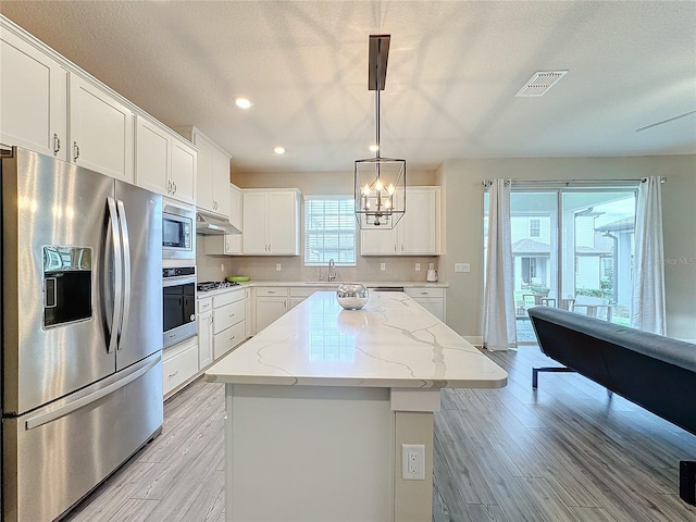 kitchen featuring a center island, hanging light fixtures, light stone countertops, white cabinetry, and stainless steel appliances