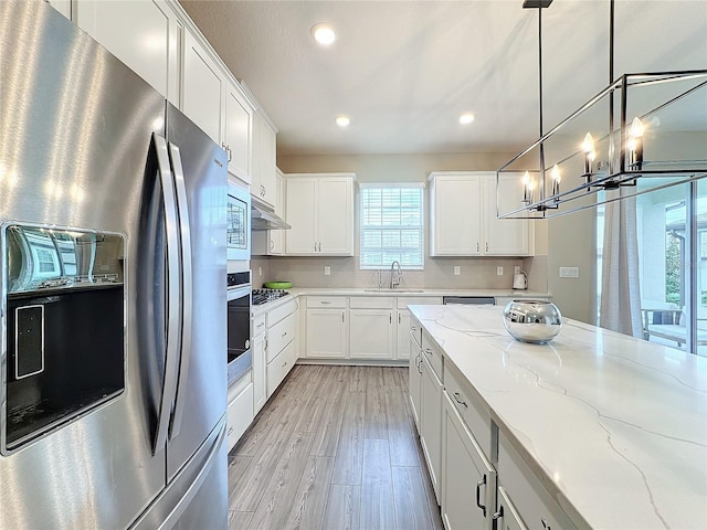 kitchen with sink, light stone counters, pendant lighting, white cabinets, and appliances with stainless steel finishes