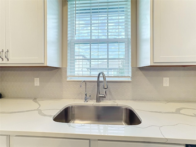 kitchen with light stone countertops, white cabinetry, sink, and tasteful backsplash