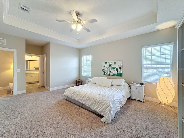 bedroom featuring ensuite bath, ornamental molding, a tray ceiling, light colored carpet, and ceiling fan