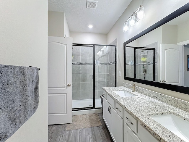 bathroom featuring a shower with door, vanity, and a textured ceiling