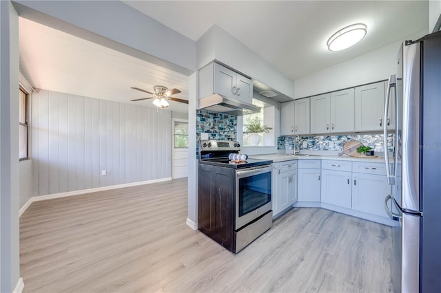 kitchen with backsplash, stainless steel appliances, ceiling fan, exhaust hood, and light hardwood / wood-style floors