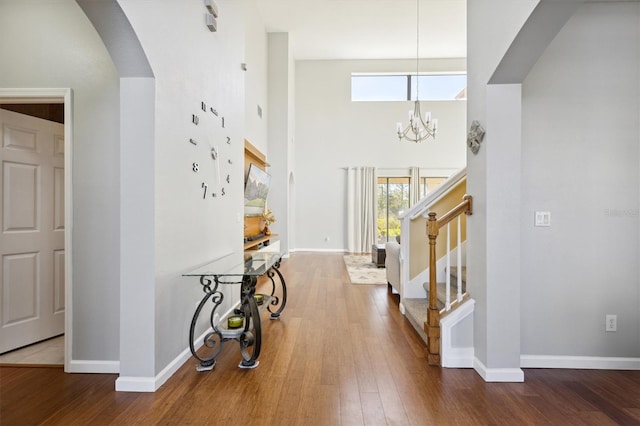 foyer entrance featuring a towering ceiling, hardwood / wood-style flooring, a wealth of natural light, and a notable chandelier