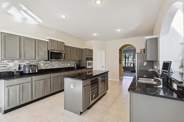 kitchen with a center island, dark stone counters, sink, appliances with stainless steel finishes, and beverage cooler