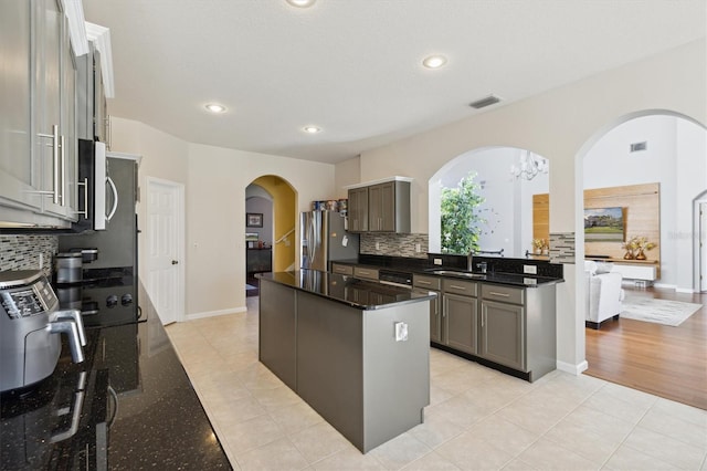 kitchen with gray cabinetry, a center island, stainless steel appliances, backsplash, and a chandelier