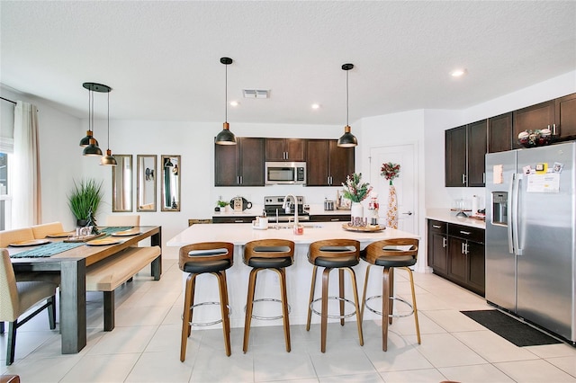 kitchen with dark brown cabinetry, an island with sink, hanging light fixtures, and appliances with stainless steel finishes