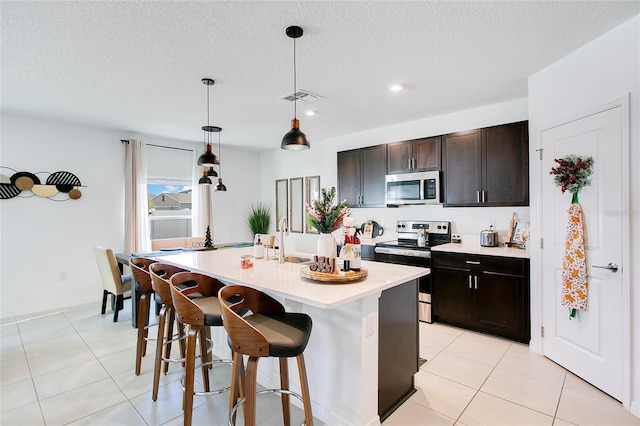 kitchen featuring an island with sink, a textured ceiling, decorative light fixtures, a breakfast bar area, and appliances with stainless steel finishes