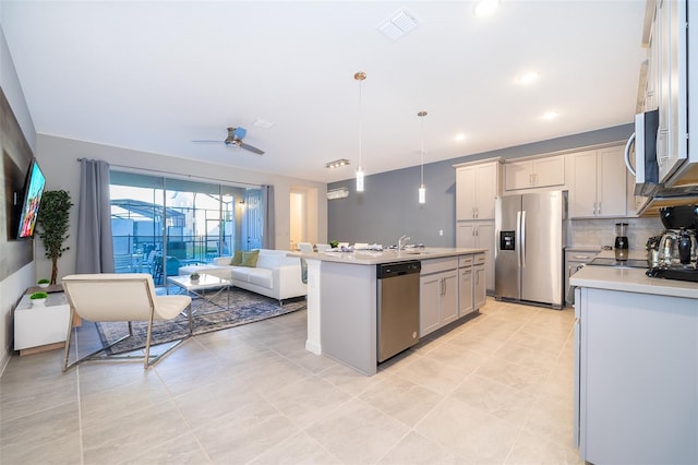 kitchen with ceiling fan, tasteful backsplash, decorative light fixtures, a center island with sink, and appliances with stainless steel finishes